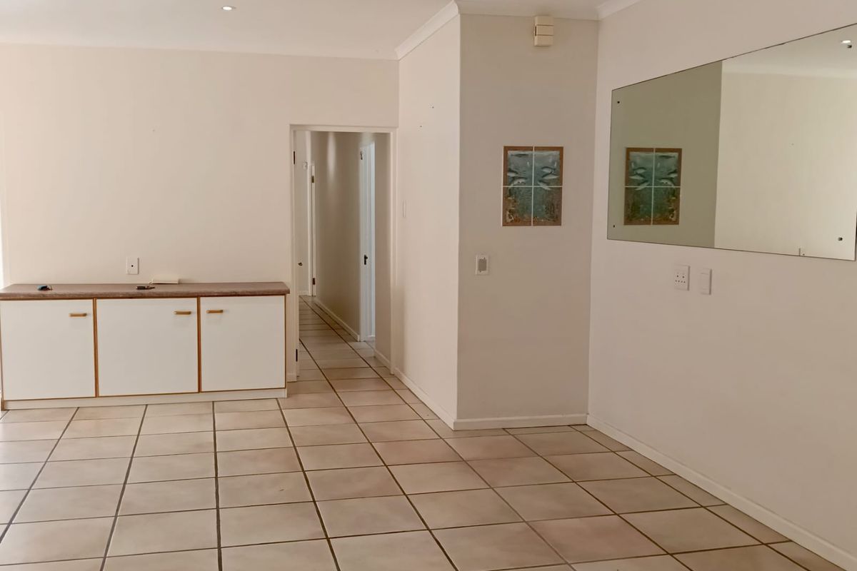 An open-plan living area featuring neutral tiled flooring, built-in cabinetry, and a large wall-mounted mirror, leading into a central hallway.