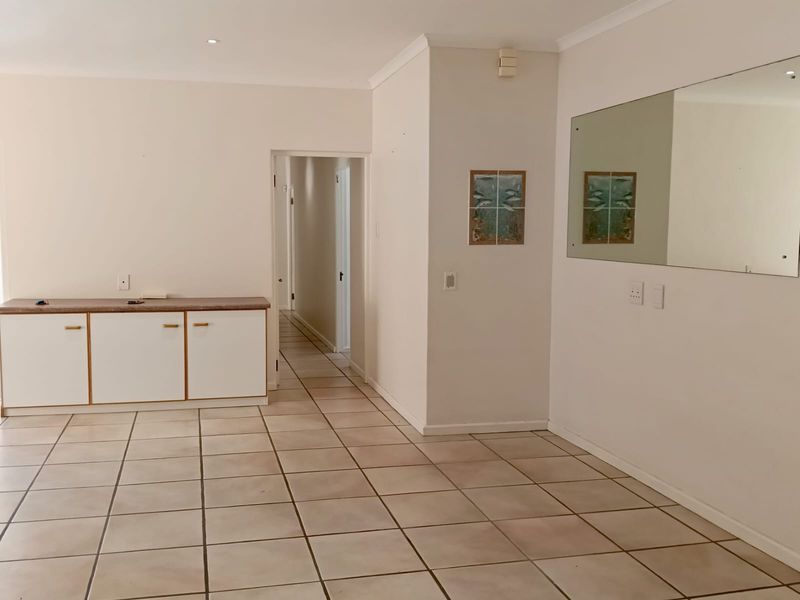 An open-plan living area featuring neutral tiled flooring, built-in cabinetry, and a large wall-mounted mirror, leading into a central hallway.