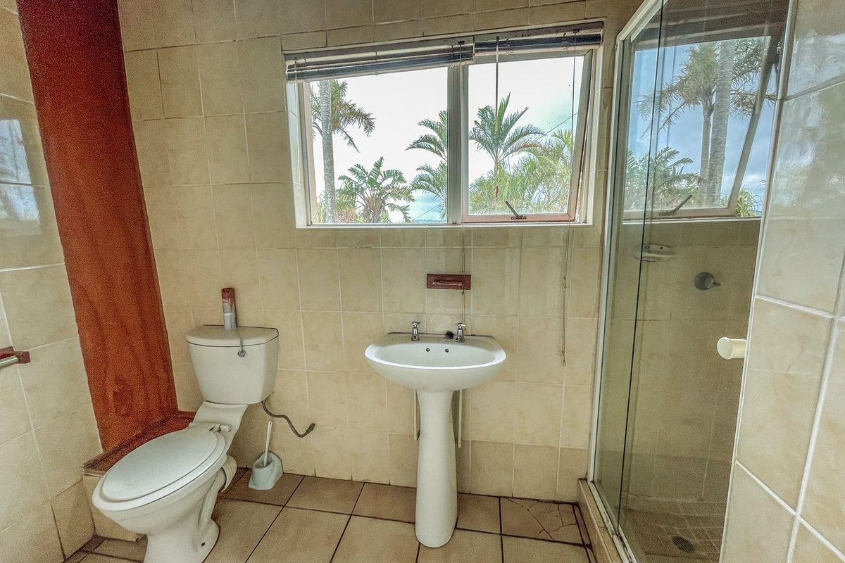 A dated bathroom featuring a pedestal basin, a standard toilet, and a glass-enclosed shower with tiled walls and flooring.