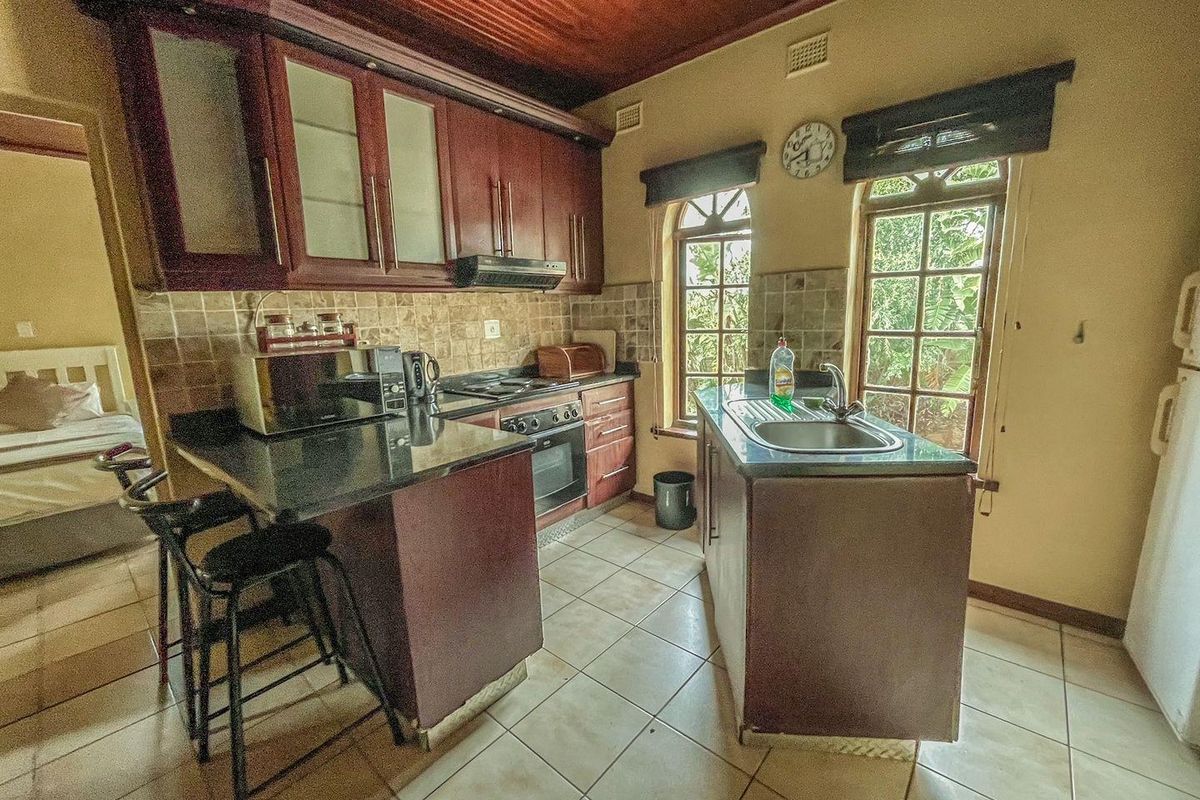 A functional kitchen featuring dark wood cabinetry, granite countertops, a built-in oven, hob, extractor fan, and a central island with a stainless steel sink.