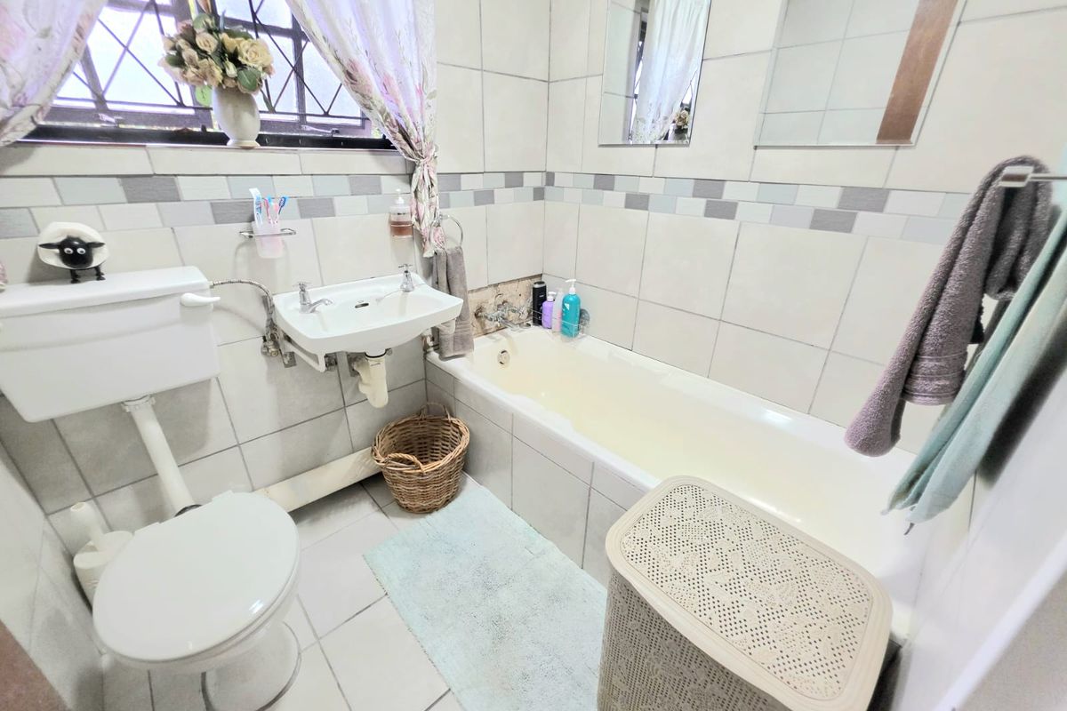 A functional bathroom featuring a bathtub, wall-mounted basin, and toilet, with tiled finishes and a window with security bars.