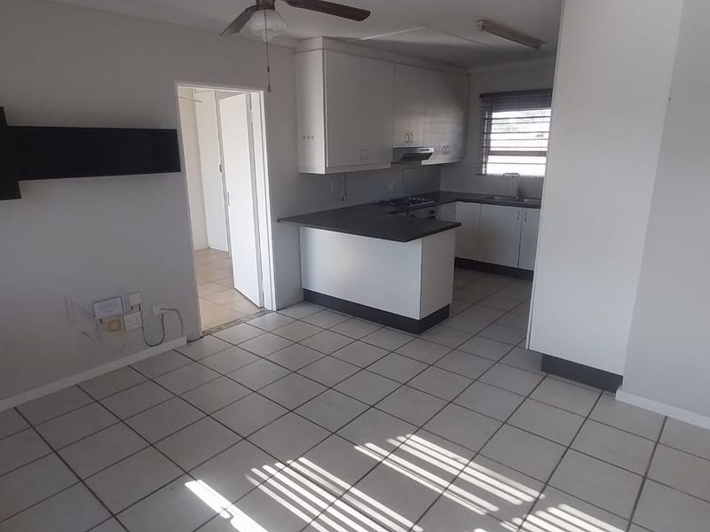 Open plan living and kitchen area featuring tiled flooring, built-in cabinetry, a breakfast bar, and a ceiling fan.