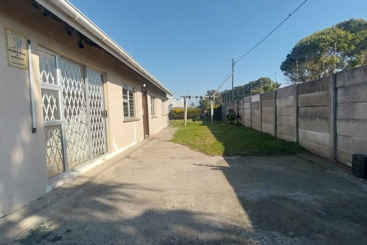 Rear exterior view showing a concrete driveway, boundary wall with electric fencing, and access to the garage and main dwelling via a sliding door.