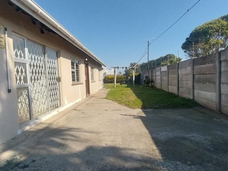 Rear exterior view showing a concrete driveway, boundary wall with electric fencing, and access to the garage and main dwelling via a sliding door.