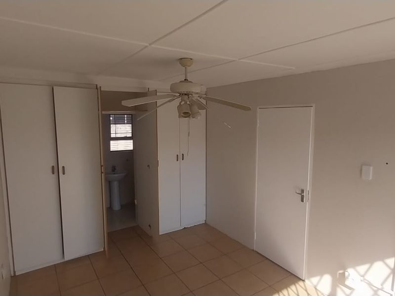 An empty bedroom featuring tiled flooring, built-in cupboards, a ceiling fan, and direct access to an en-suite bathroom.