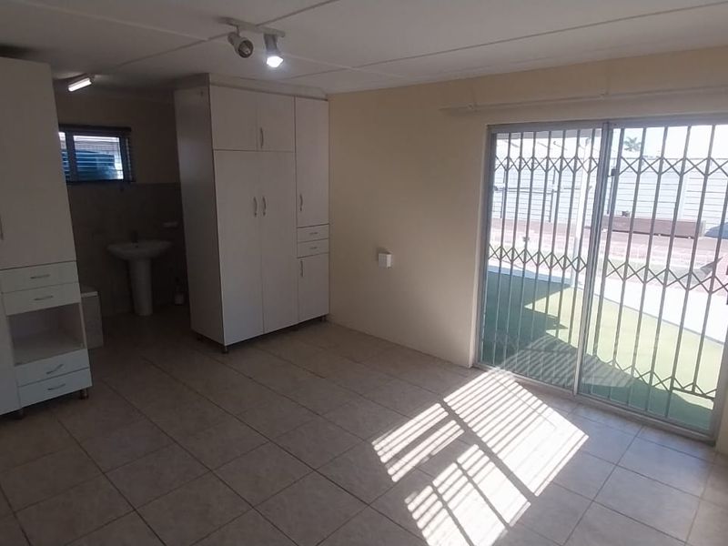 A bright, empty bedroom featuring built-in cupboards, tiled flooring, and a sliding glass door with a security gate leading to the exterior.