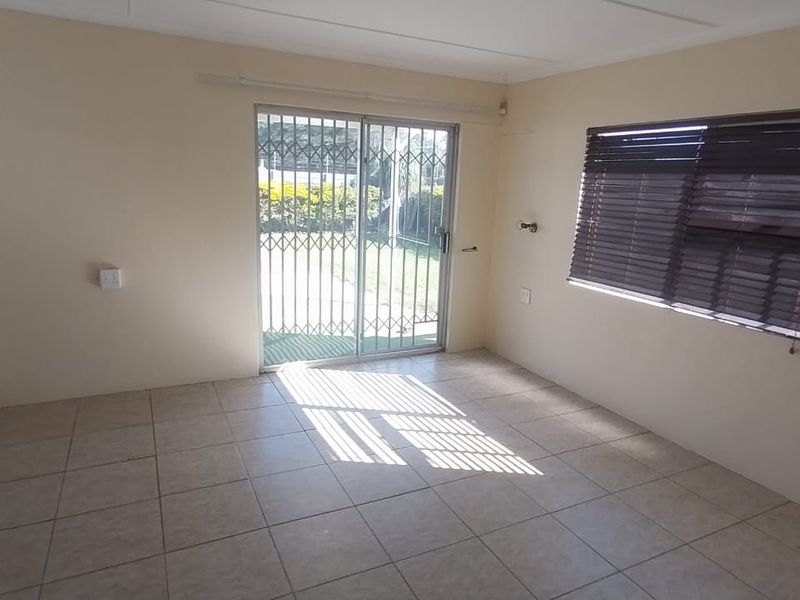 A bright, empty bedroom featuring tiled flooring, a built-in wardrobe, and a sliding glass door with a security gate leading to the garden.