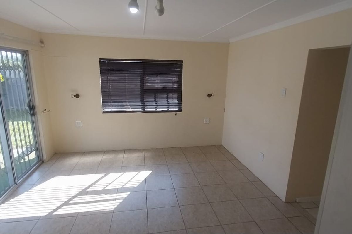 An empty living room featuring tiled flooring, a sliding glass door with security gate, and a window with fitted blinds.