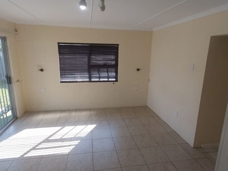 An empty living room featuring tiled flooring, a sliding glass door with security gate, and a window with fitted blinds.