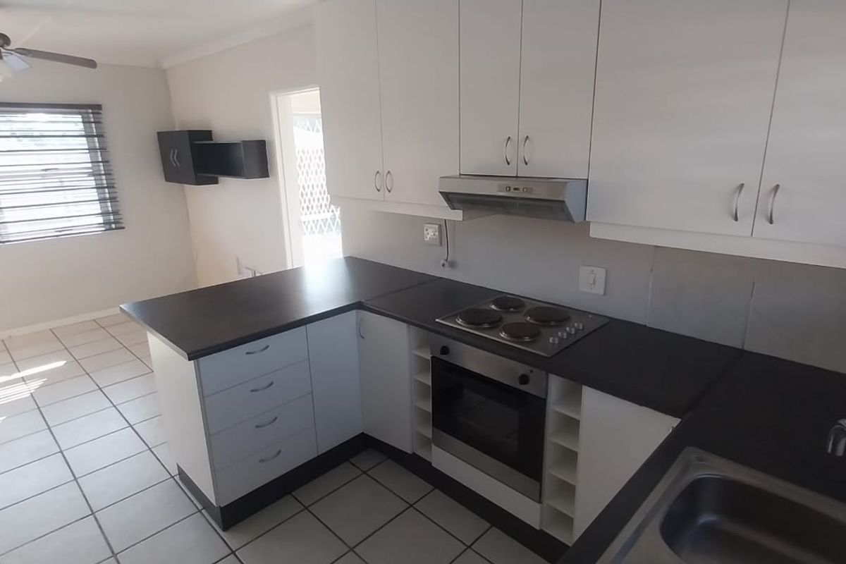 A clean, functional kitchen featuring white cabinetry, dark countertops, built-in oven and hob, and tiled flooring in an open-plan layout.