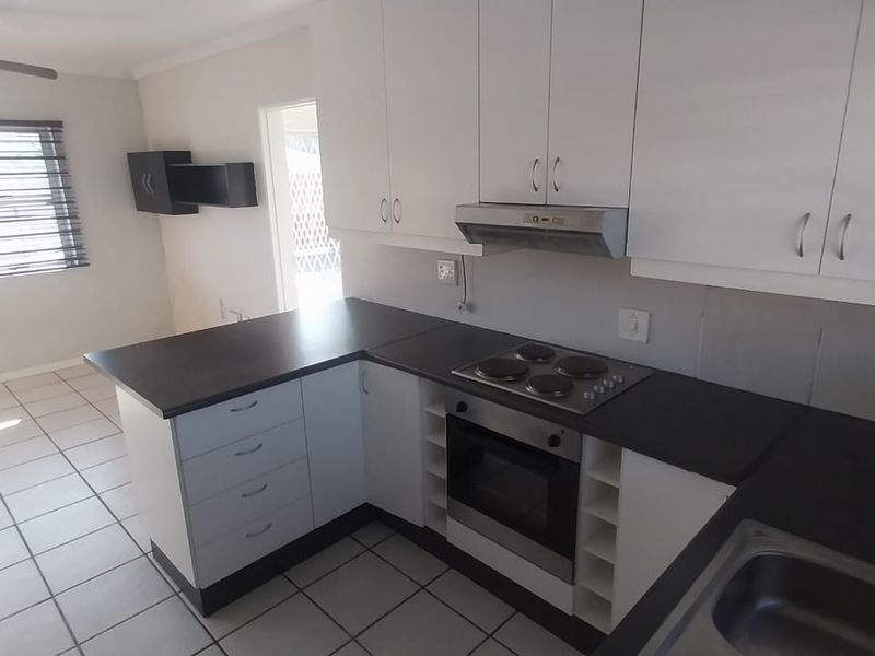 A clean, functional kitchen featuring white cabinetry, dark countertops, built-in oven and hob, and tiled flooring in an open-plan layout.