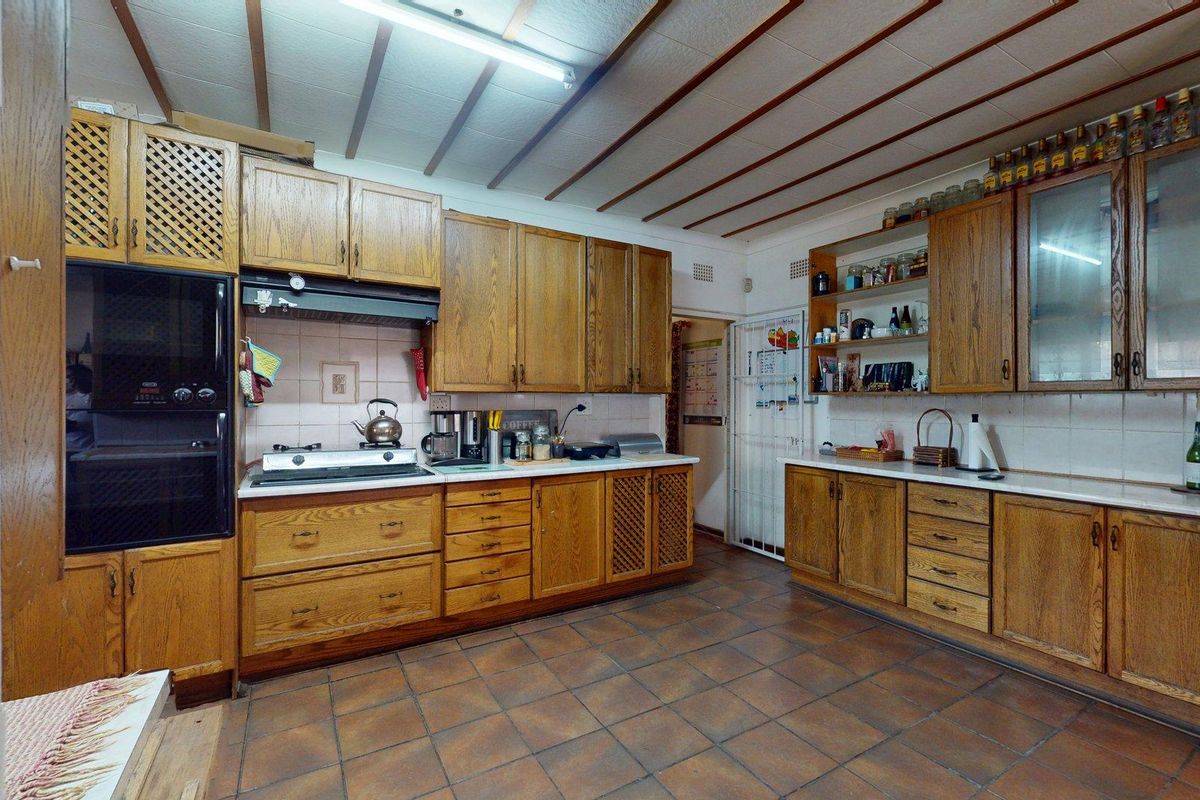 A spacious kitchen featuring extensive wooden cabinetry, tiled flooring, a built-in oven, and a gas hob, offering a functional layout with a dated aesthetic.