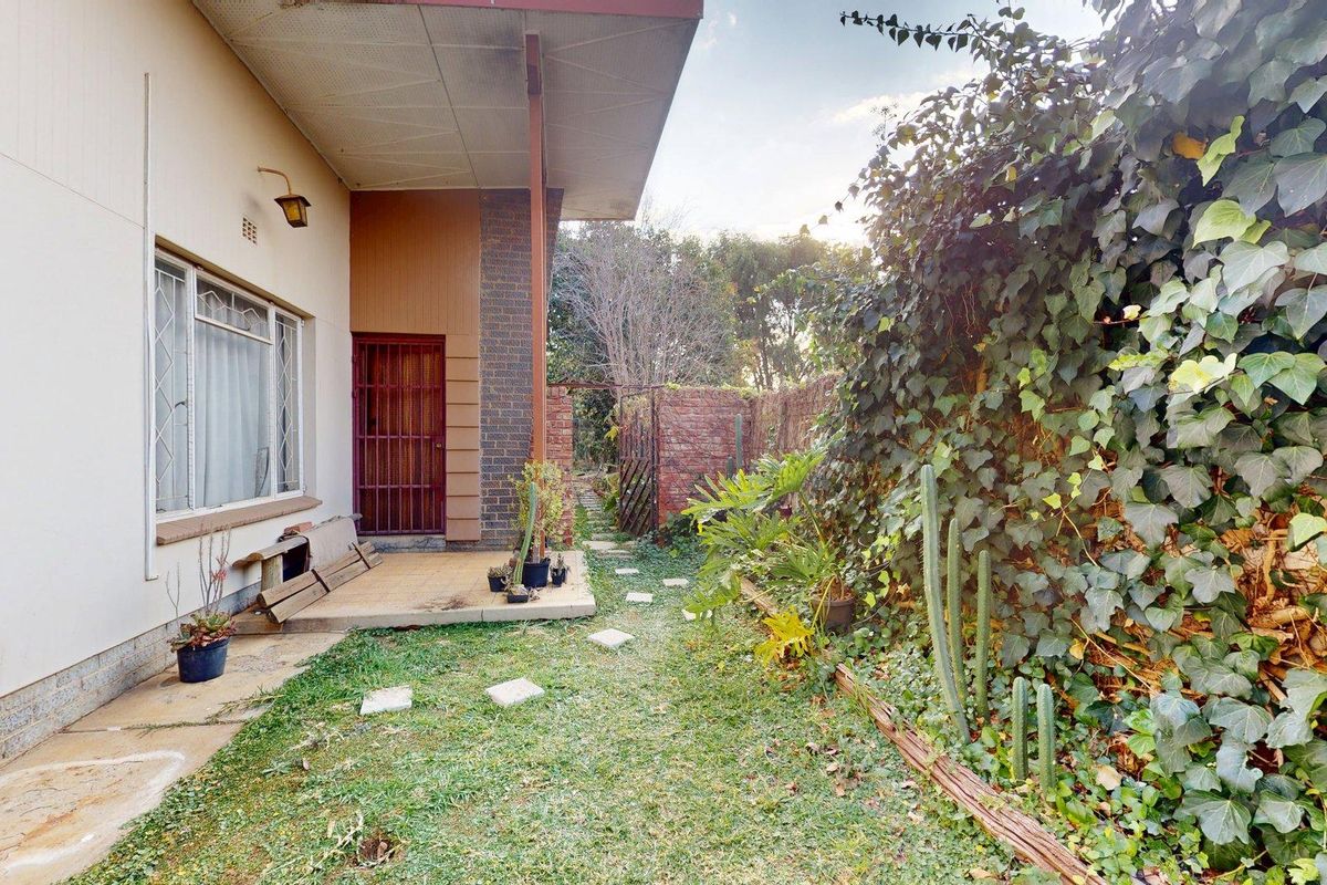 A rear exterior view featuring a small tiled patio area, brick boundary wall, and established garden space with mature climbing ivy.
