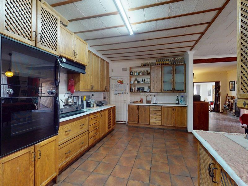 Spacious kitchen featuring extensive wooden cabinetry, built-in oven, cooktop, and tiled flooring, offering a functional layout with potential for modern updates.