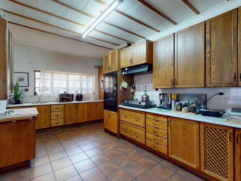 A spacious, dated kitchen featuring extensive wooden cabinetry, tiled flooring, and a functional layout with built-in appliances and ample counter space.