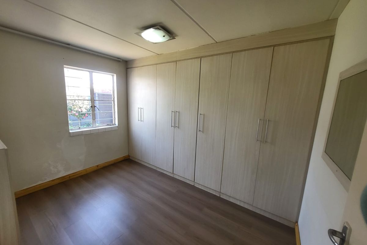 A vacant bedroom featuring extensive built-in cupboards, laminate flooring, and a window with security bars, ready for personalization.
