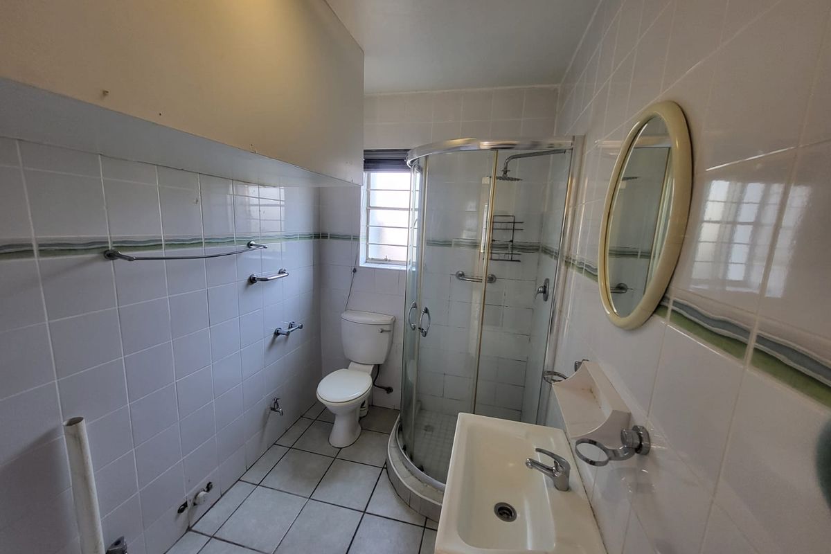 A functional bathroom featuring a corner shower, pedestal basin, and toilet, finished with white wall tiles and floor tiling.