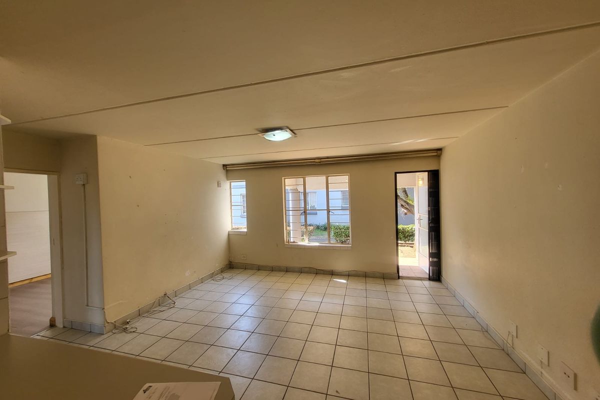 An empty, open-plan living area featuring ceramic floor tiles, security bars on windows, and a security gate leading to the exterior.