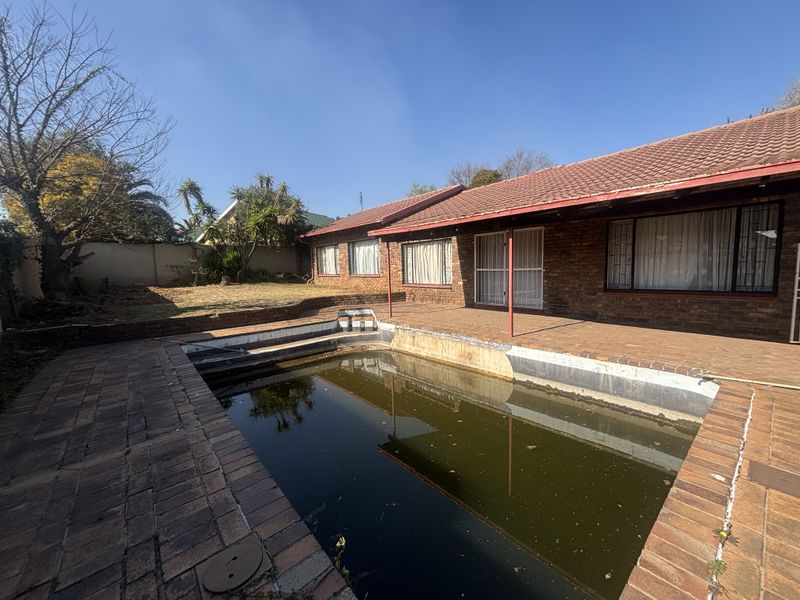 Rear exterior view featuring a brick-paved patio area and a swimming pool requiring maintenance and cleaning.