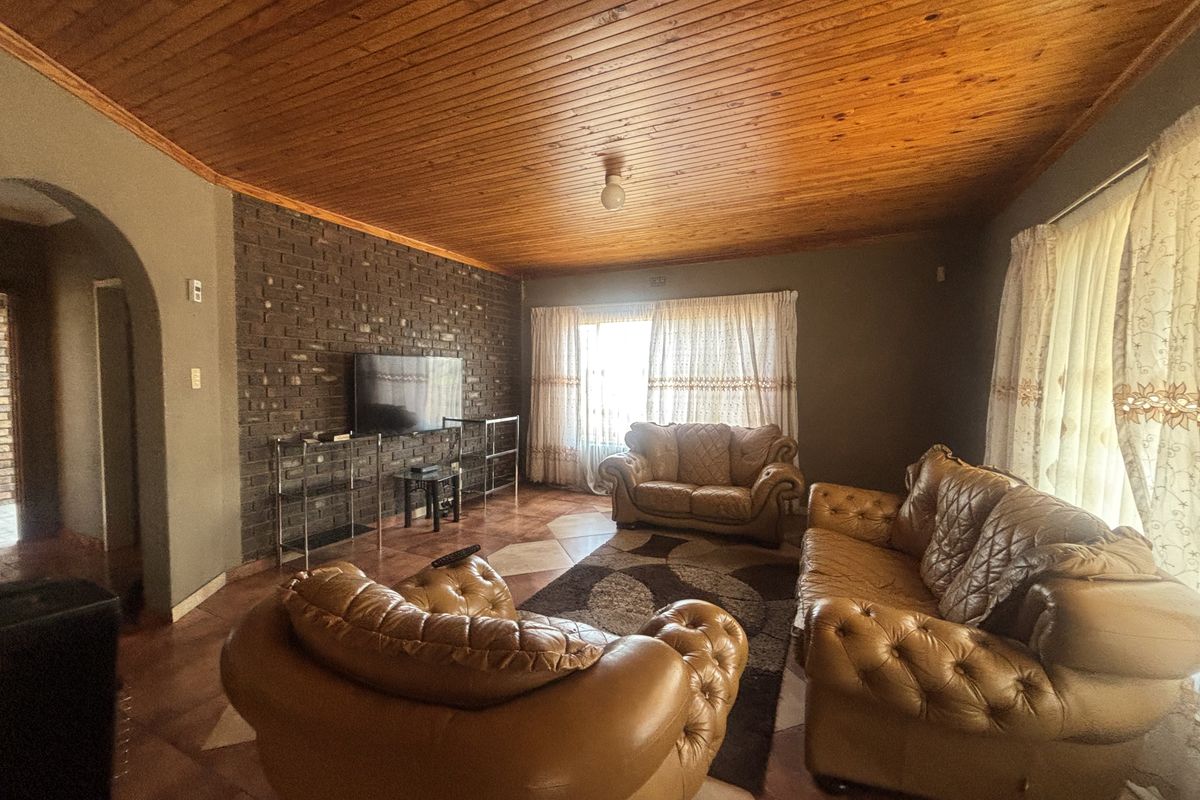 A living room featuring a distinctive exposed brick wall, warm timber ceiling, and tiled flooring, offering a cozy and traditional aesthetic.