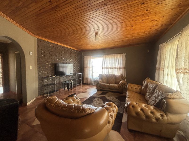 A living room featuring a distinctive exposed brick wall, warm timber ceiling, and tiled flooring, offering a cozy and traditional aesthetic.