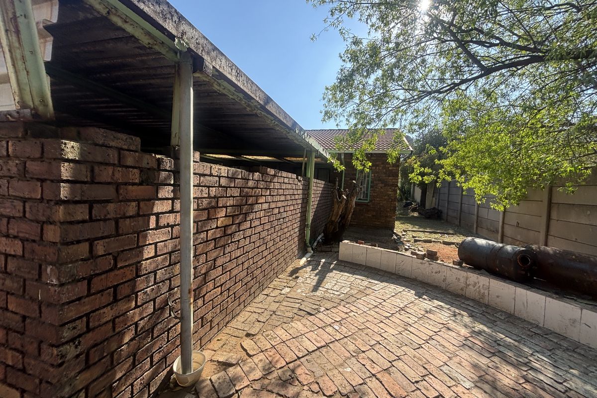 Rear exterior area featuring a brick boundary wall, paved ground surface, and a weathered corrugated metal lean-to structure.