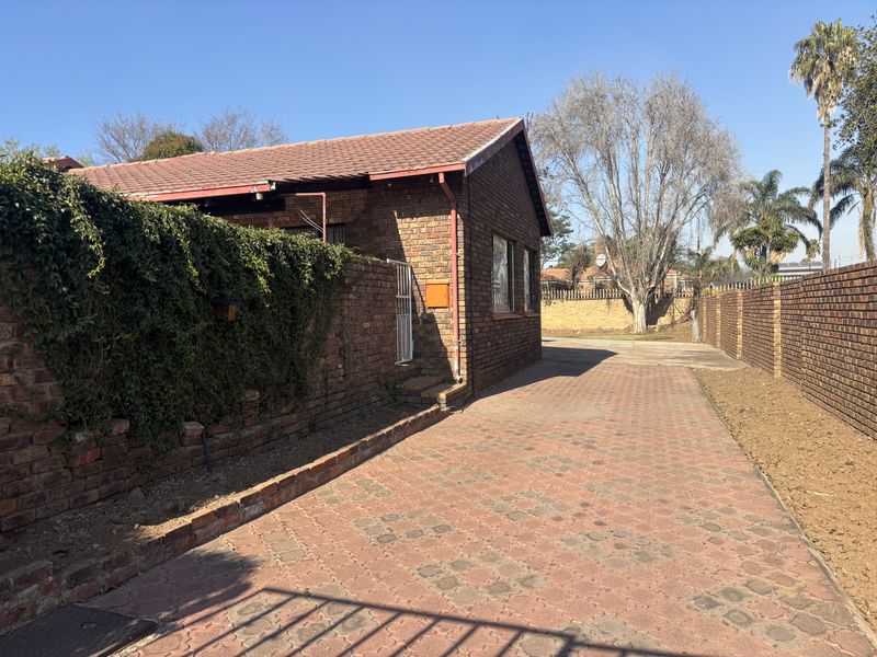Exterior view of a face brick house featuring a paved driveway, secure boundary walls, and a tiled roof.