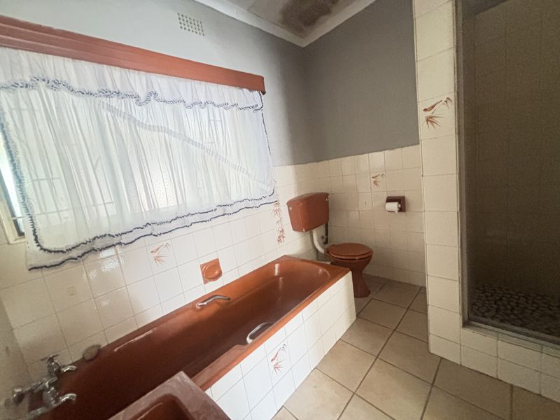 A dated bathroom featuring a built-in bathtub, toilet, and shower enclosure with original ceramic tiling and visible ceiling water damage.
