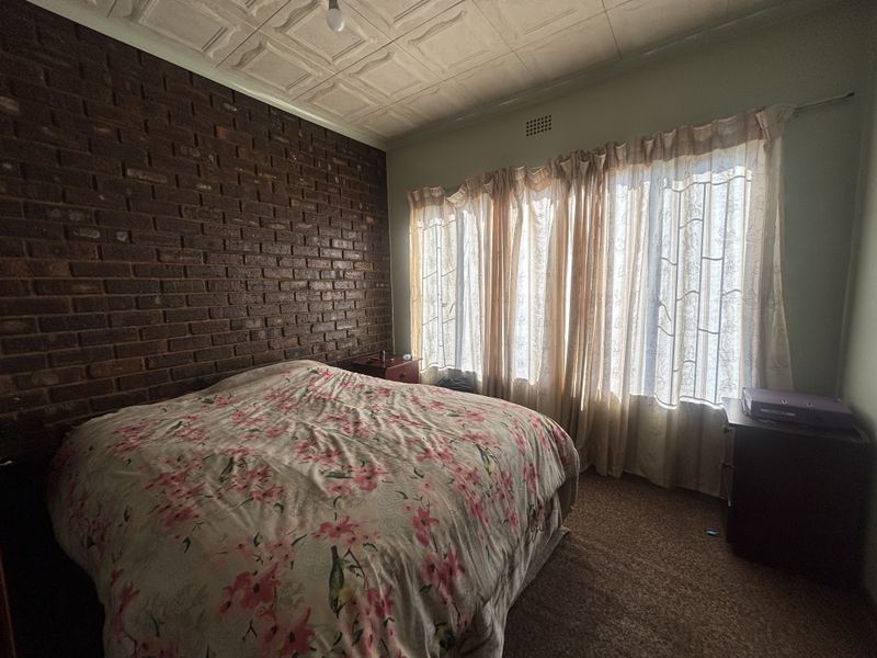 Bedroom featuring an exposed brick feature wall, pressed metal ceiling, and carpet flooring, offering a classic aesthetic with potential for modern updates.