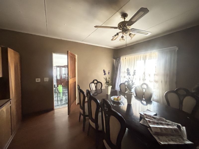 A dining room featuring laminate flooring, a ceiling fan, and access to an adjacent room through a timber door.