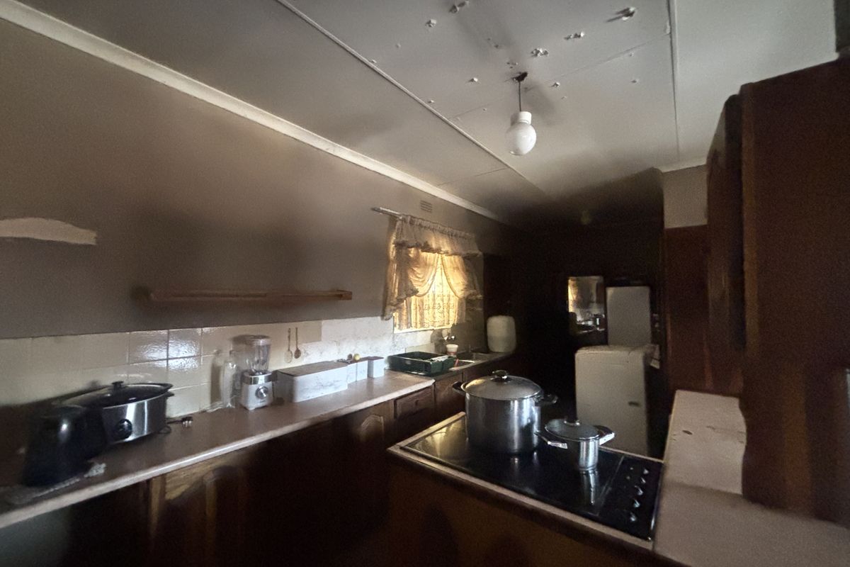 A dated kitchen featuring original cabinetry, laminate countertops, and a built-in cooktop, requiring significant cosmetic updates and ceiling repairs.