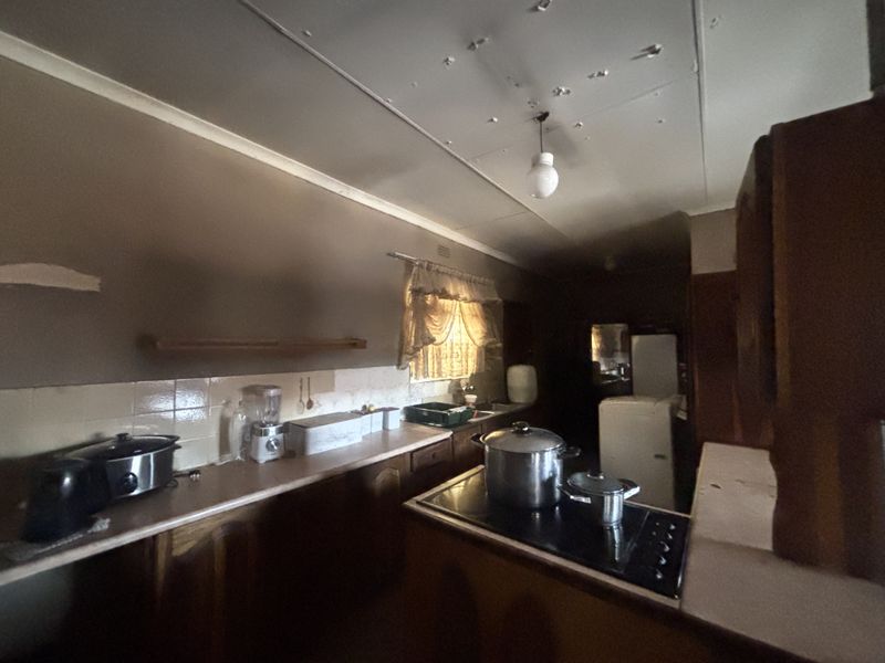 A dated kitchen featuring original cabinetry, laminate countertops, and a built-in cooktop, requiring significant cosmetic updates and ceiling repairs.