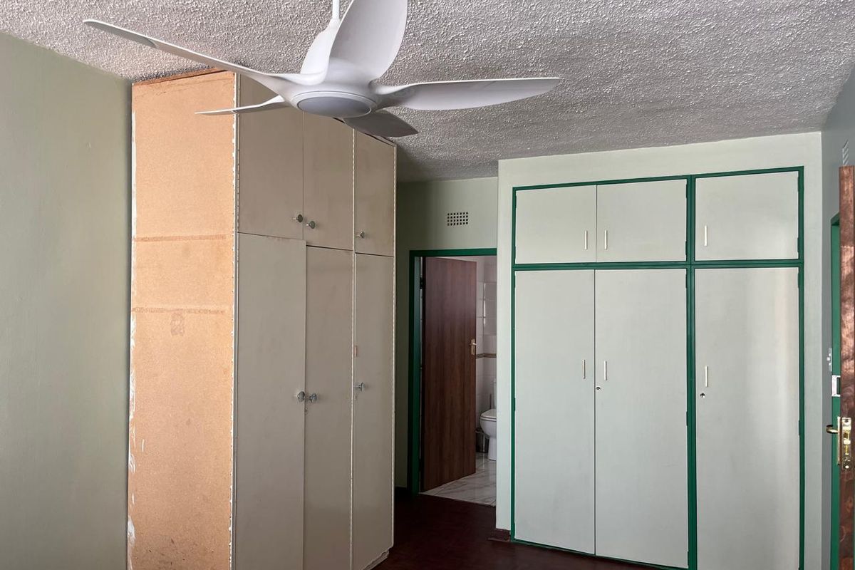 Bedroom featuring built-in cupboards, a ceiling fan, and textured ceiling, offering a functional space ready for cosmetic updates.
