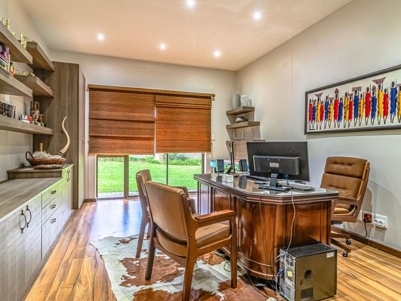 A well-appointed home office featuring custom built-in cabinetry, floating shelving, laminate flooring, and direct access to the garden through a sliding glass door.