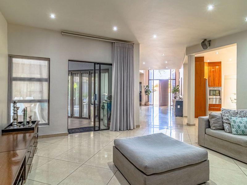 Spacious open-plan living area featuring polished tile flooring, recessed lighting, and seamless flow to the kitchen and outdoor patio through sliding glass doors.