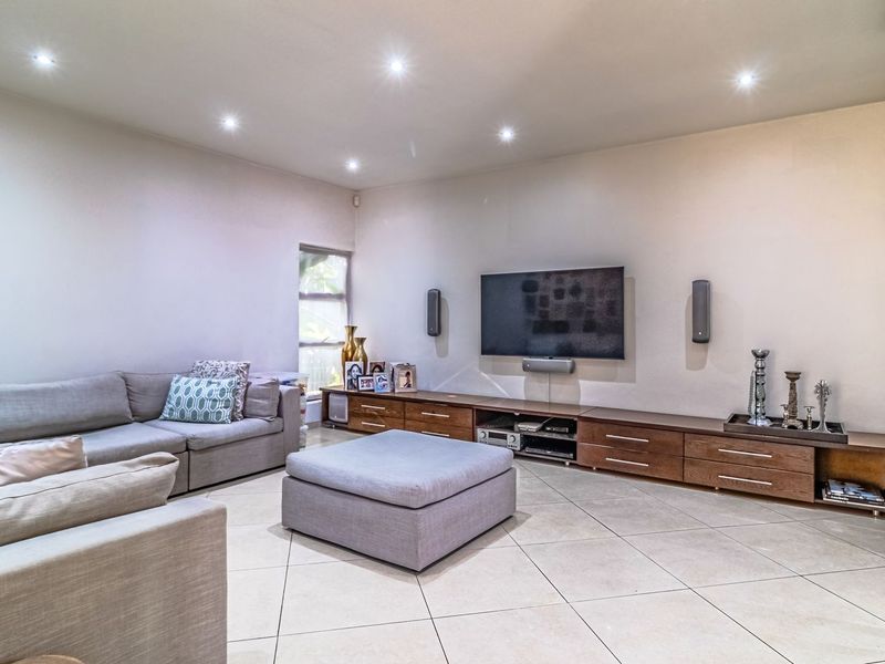 Spacious living room featuring neutral tiled flooring, recessed downlighting, and extensive built-in cabinetry for media storage.