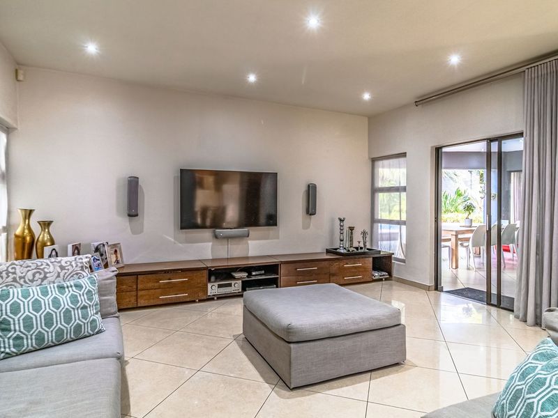 Spacious living room featuring neutral tiled flooring, recessed downlighting, and large sliding glass doors providing seamless access to the outdoor patio area.