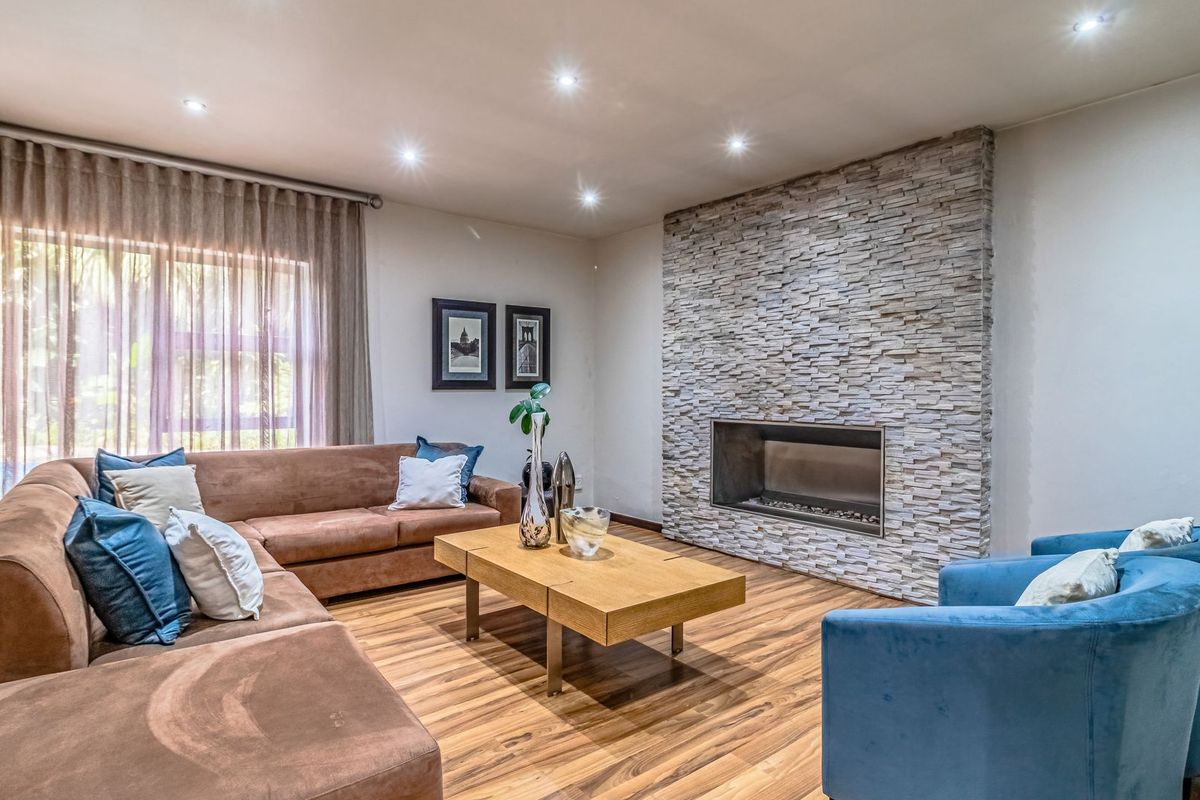 A well-maintained living room featuring a prominent stone-clad fireplace, recessed downlighting, and warm-toned laminate flooring.