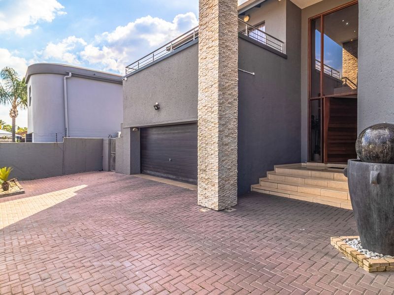 Modern front facade featuring a paved driveway, stone-clad architectural pillar, double-volume entrance, and an integrated garage.
