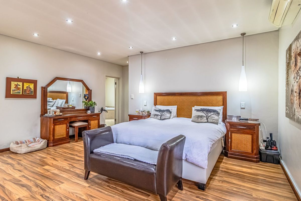 Spacious bedroom featuring warm-toned laminate flooring, recessed downlighting, and a wall-mounted split-system air conditioner for climate control.