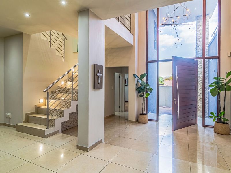 Spacious double-volume entrance hall featuring large windows, modern tiled flooring, and a contemporary staircase with metal balustrades.