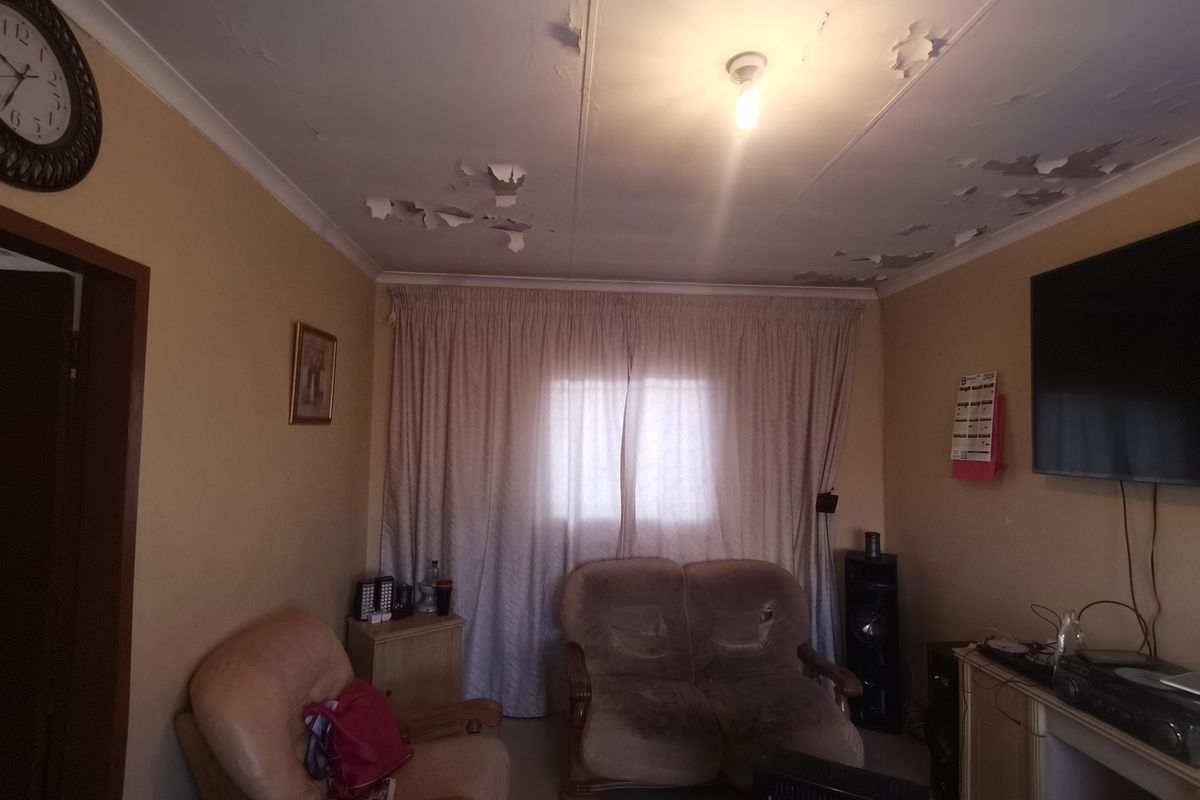 A living room featuring a window with curtain tracks and a ceiling requiring maintenance due to significant paint peeling and surface damage.