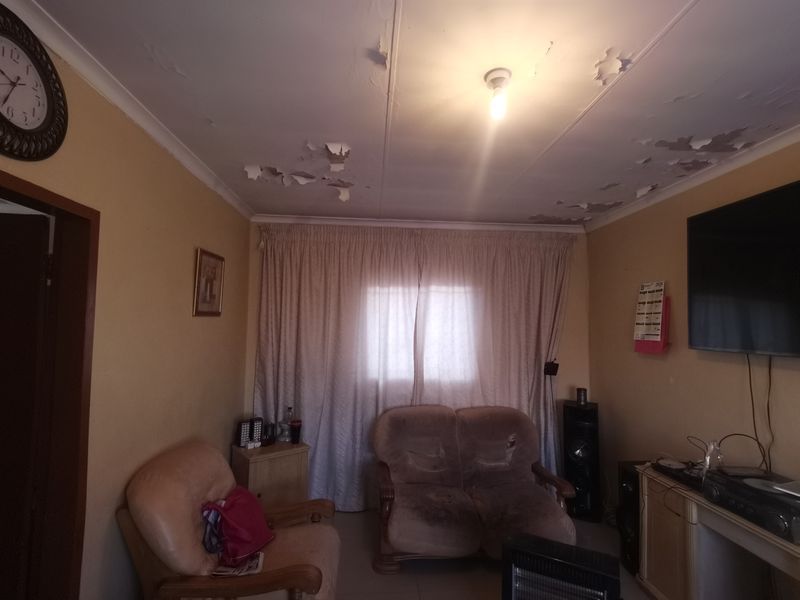 A living room featuring a window with curtain tracks and a ceiling requiring maintenance due to significant paint peeling and surface damage.