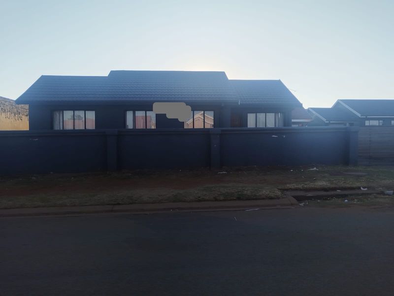 Front elevation of a single-story house featuring a dark-painted perimeter wall, tiled roof, and aluminium window frames.
