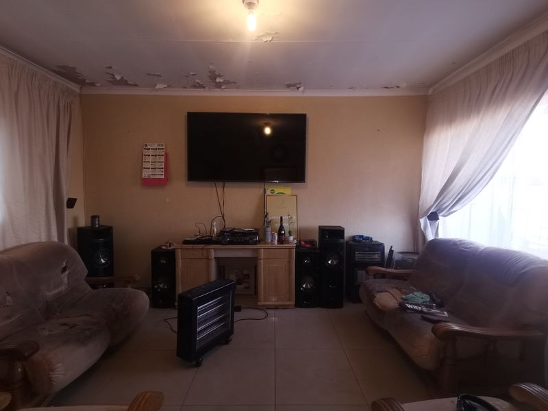 A living room featuring tiled flooring and a ceiling in need of repair due to significant paint peeling.