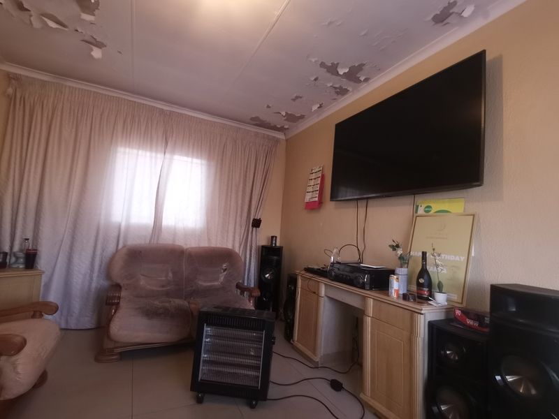 A living room area featuring tiled flooring, currently showing significant signs of wear including peeling paint on the ceiling.