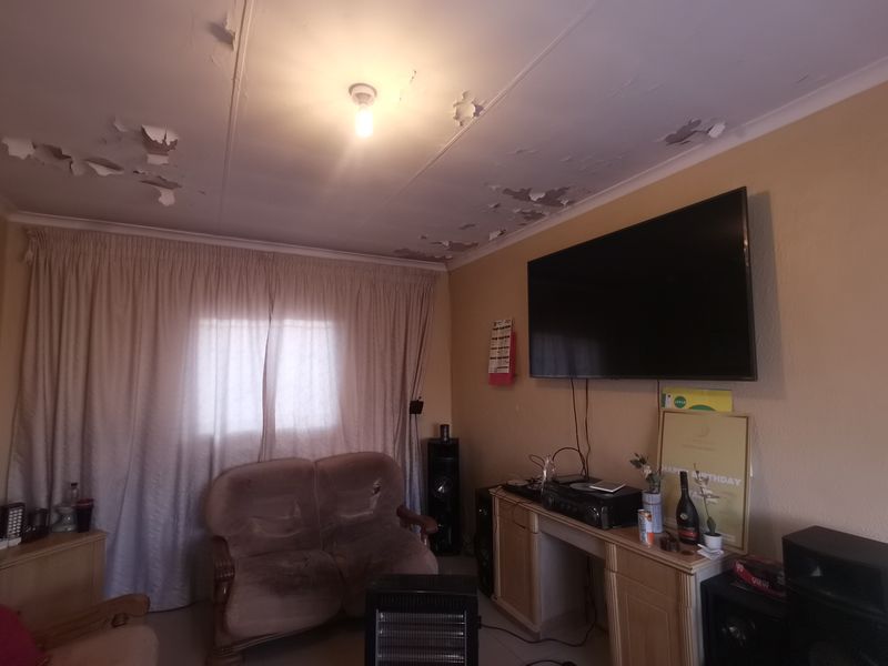 A living room space featuring a wall-mounted television area and significant ceiling paint deterioration requiring maintenance and repair.
