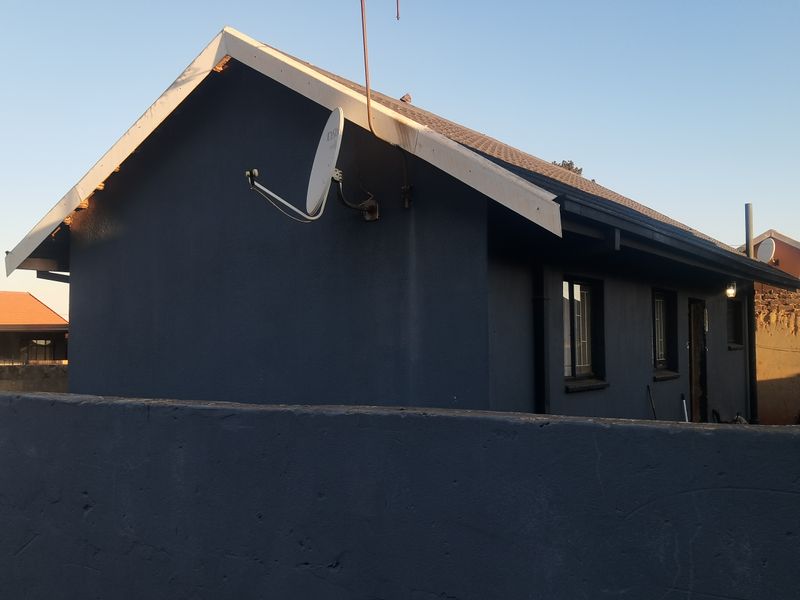 Rear view of the property featuring a dark-painted exterior, tiled roof, and a boundary wall, showing signs of general wear on the fascia boards.