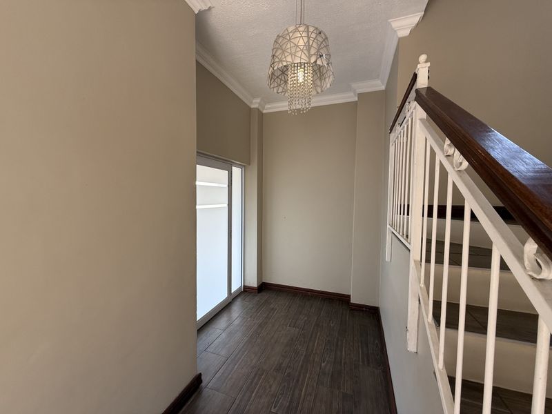 A bright and spacious entrance hall featuring tiled flooring, crown molding, and a staircase with a wooden handrail and metal balustrade.