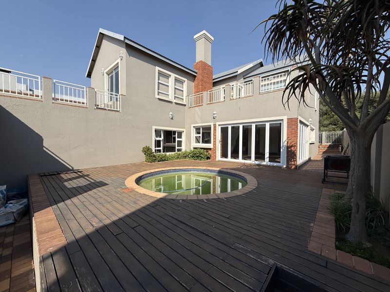 Rear exterior view featuring a circular swimming pool set within a timber deck, adjacent to a two-story residence with balcony access and brick chimney.